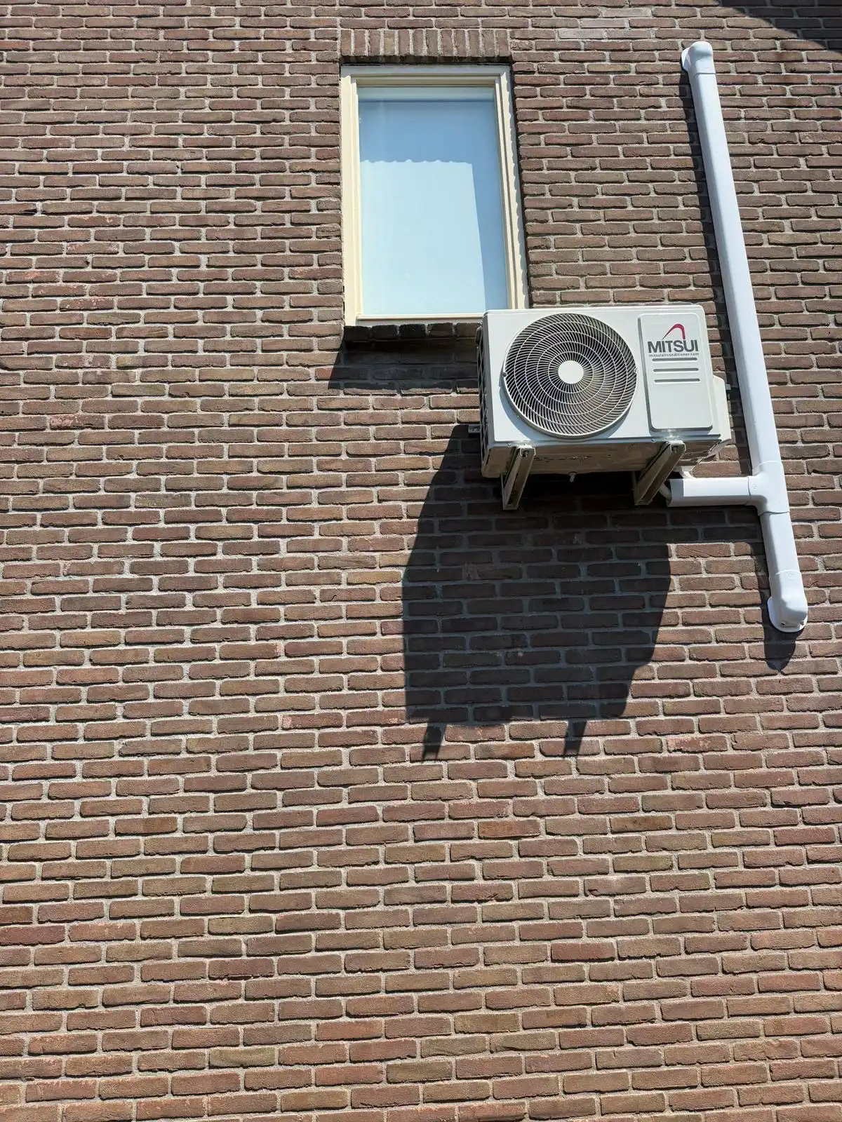 Mitsui airco buitenunit netjes op houten beugels aan een bakstenen gevel gemonteerd