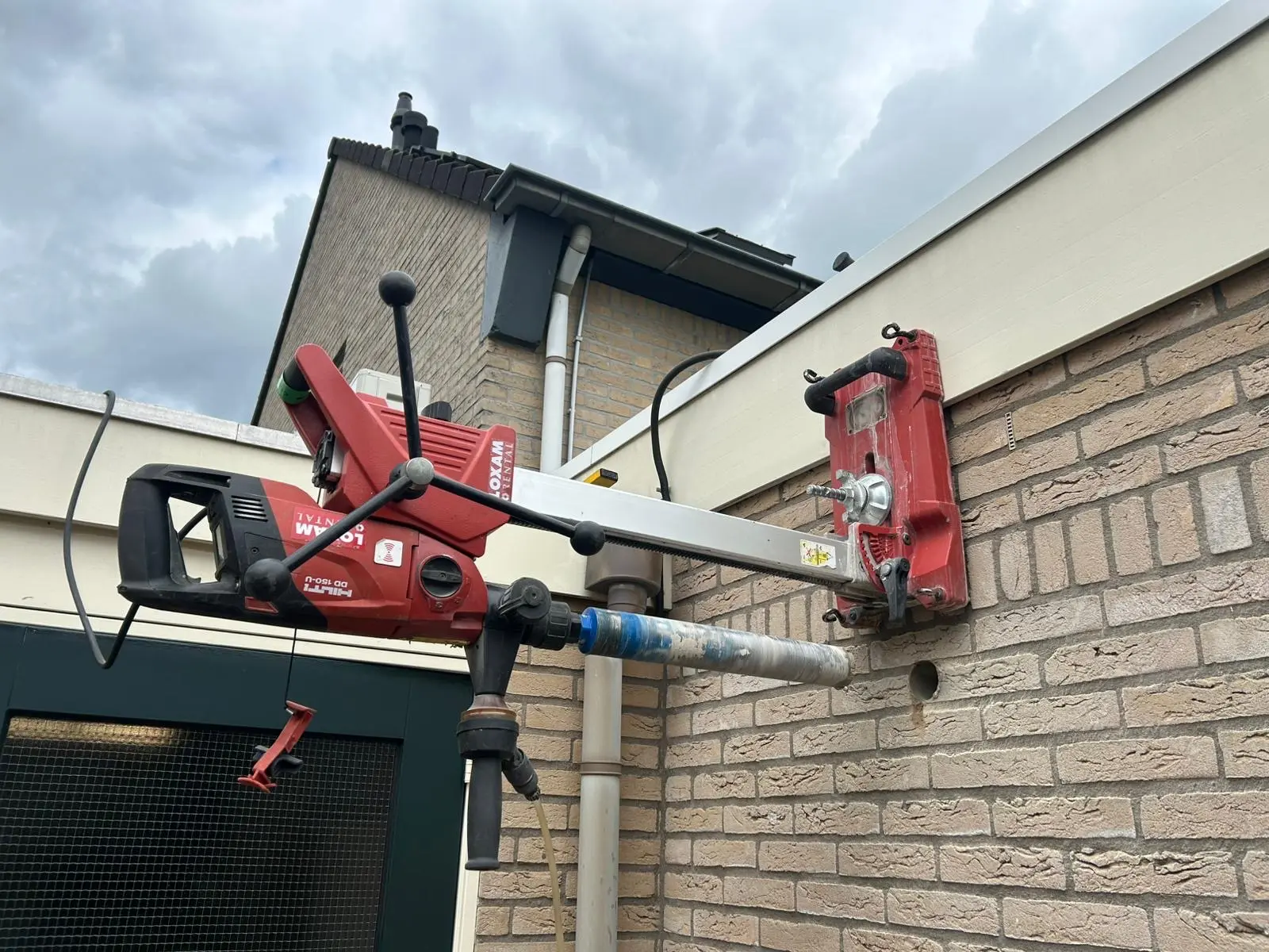 Hilti diamantboorstatief verankerd aan een bakstenen gevel tijdens het boren van een ventilatiegat