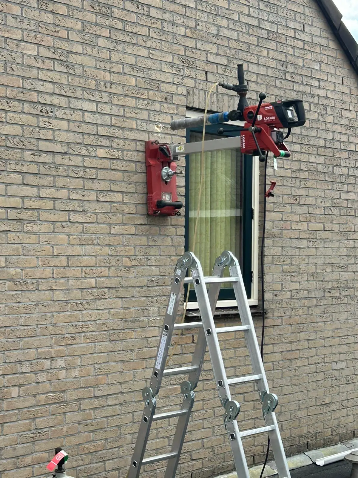 Diamantboormachine met kernboor in een lichte bakstenen gevel, met de wateraanvoer aangesloten