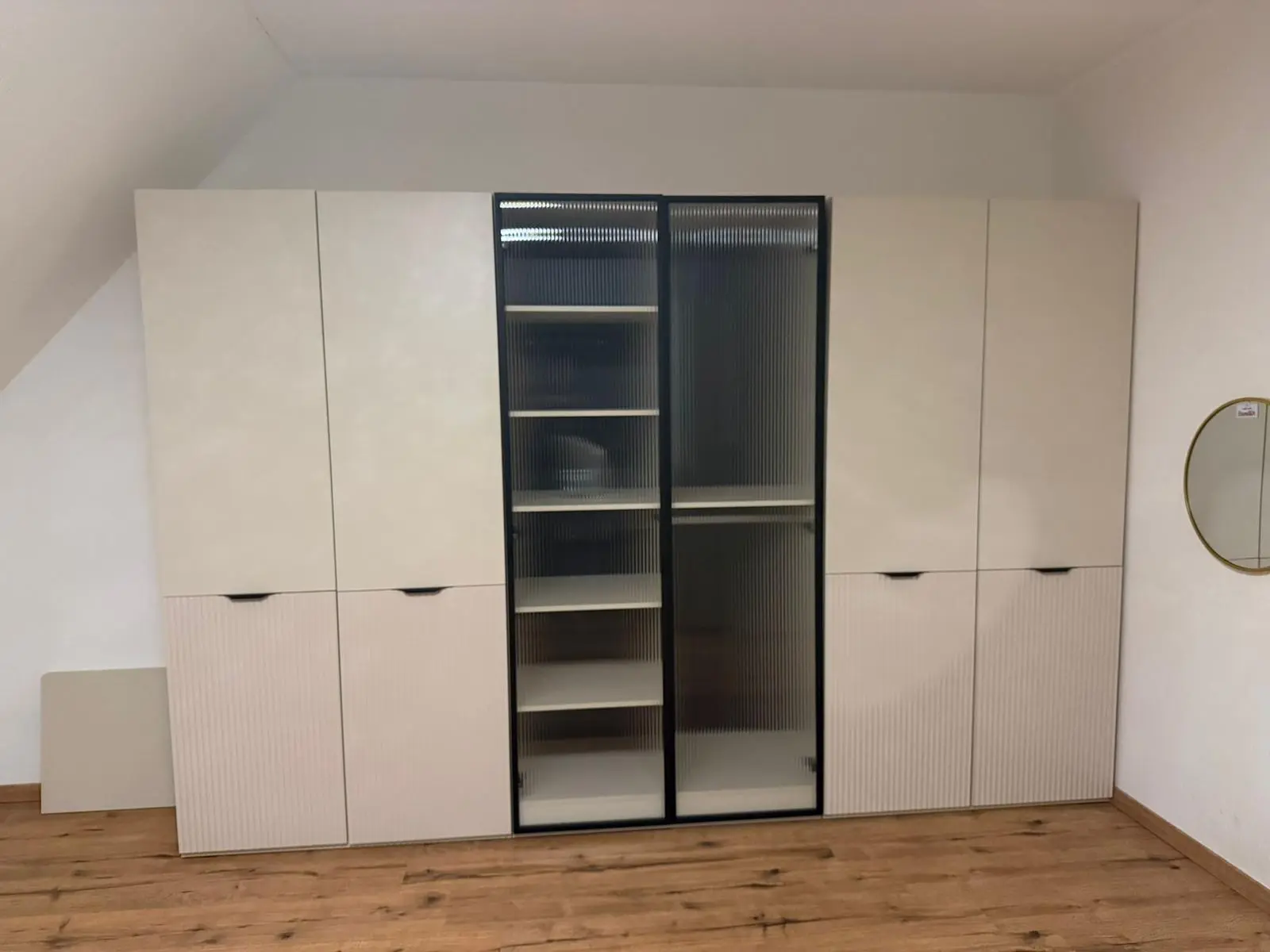 Op maat gemonteerde witte inbouwkast met ribbelfronten en geribbelde glazen deuren onder een schuine wand