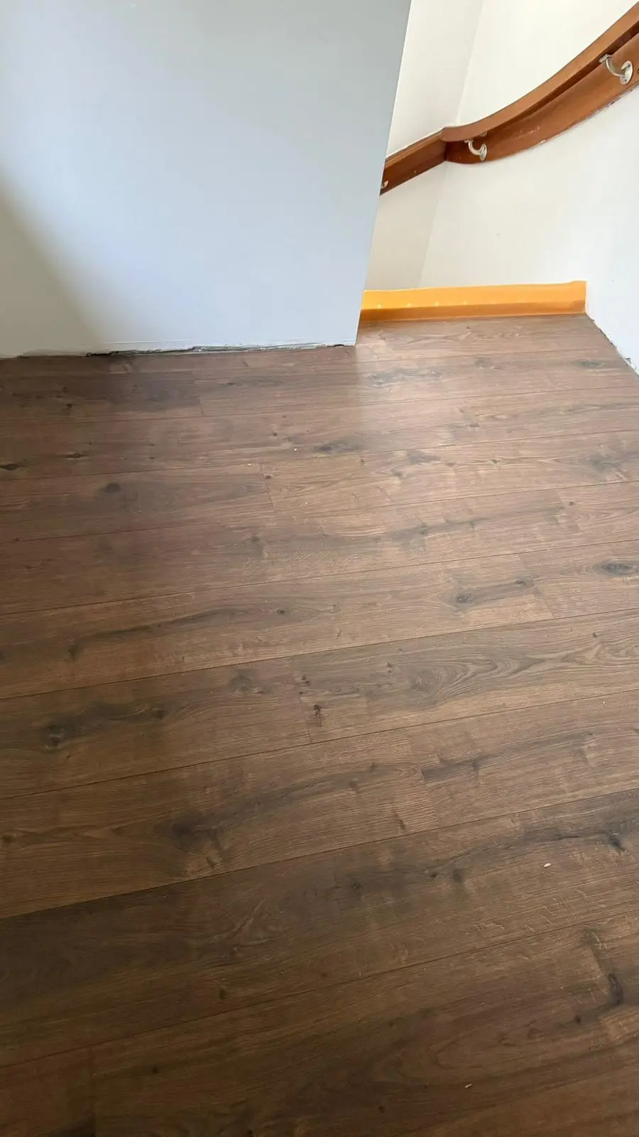 Donkere laminaatvloer op een overloop, netjes afgewerkt langs de trap en de leuning